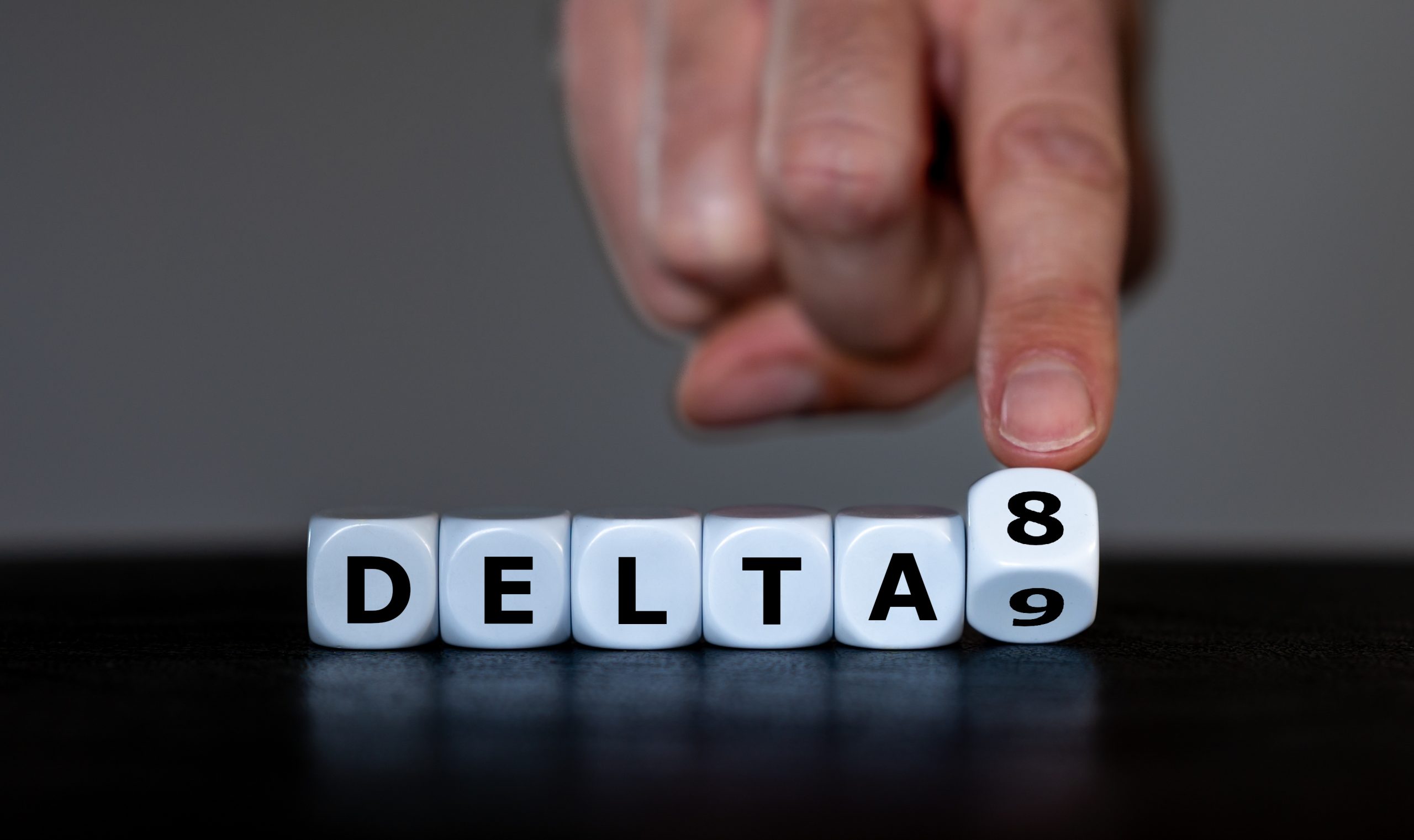 Hand turns dice and changes the expression 'delta 9' to 'delta 8'. Symbol for the Delta-8-tetrahydrocannabinol, a psychoactive cannabinoid found in the Cannabis plant.